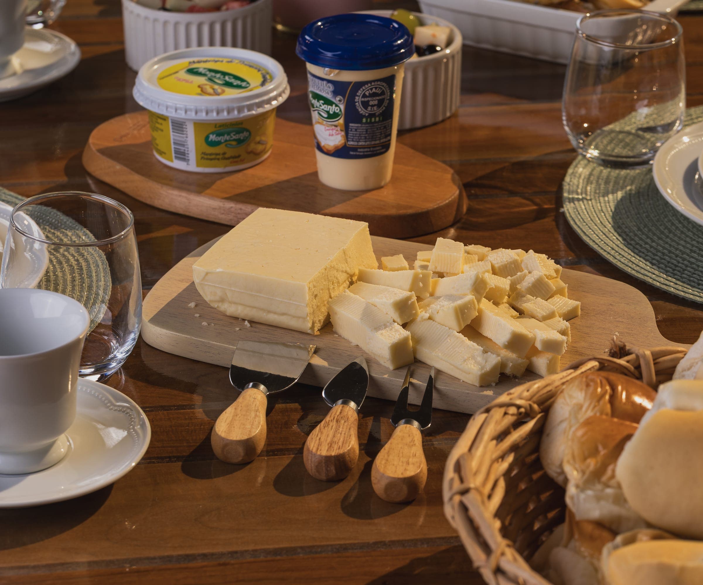 Mesa de café da manhã com requeijão e manteiga MonteSanto, queijo em cubos na tábua, pães e café